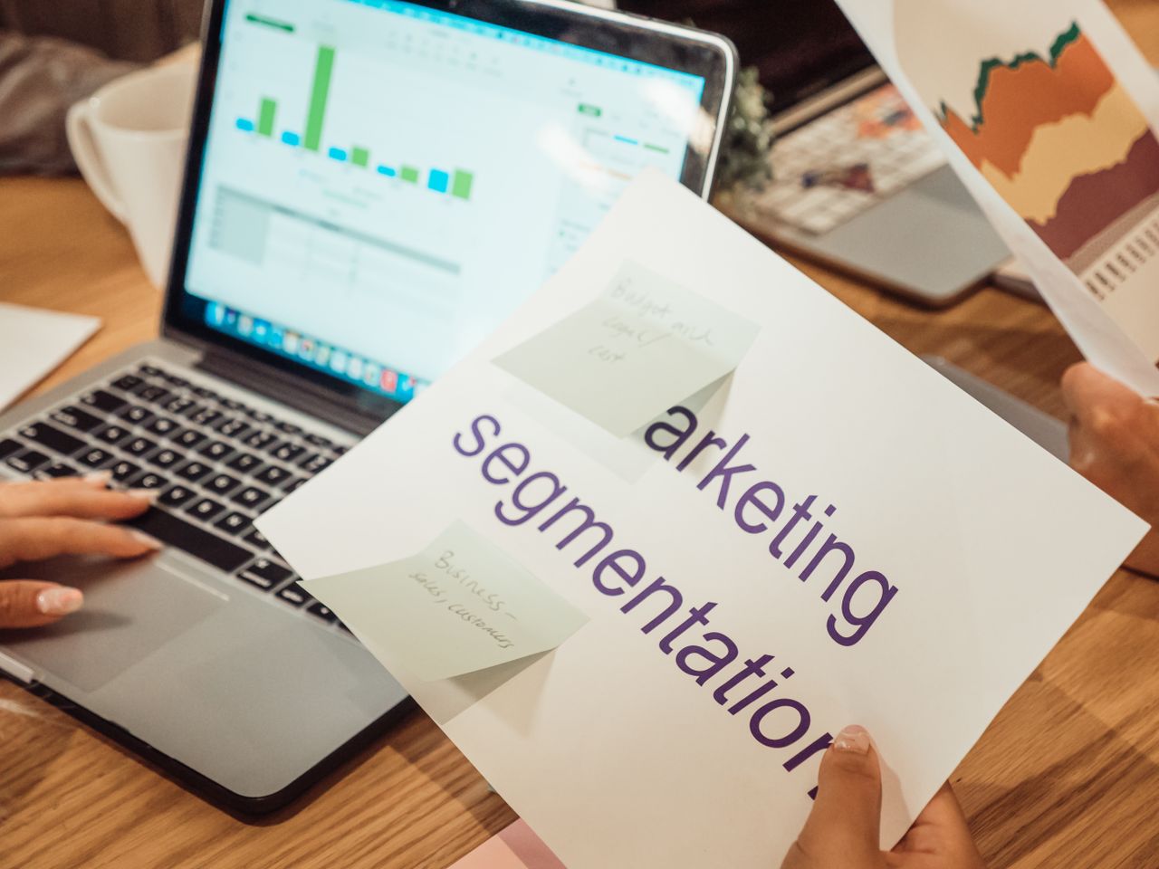 Un espace de travail moderne où des mains analysent des données marketing sur un ordinateur portable et des documents papier.